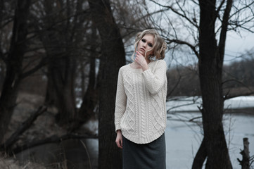 beautiful young  blonde woman with blue eyes in white pullover long skirt on spring background, forest, lake, trees. Cold mood. Fashion, emotional portrait..Winter, spring, outdoor portrait. 