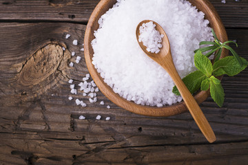 Large White sea salt in a natural wooden bowl with  sprig of fresh rosemary on  simple  background. Selective focus.