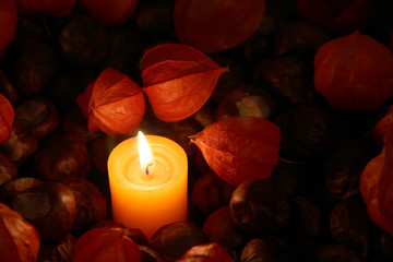 Kerze brennt im Dunkeln zwischen Kastanien und Lampions im Herbst