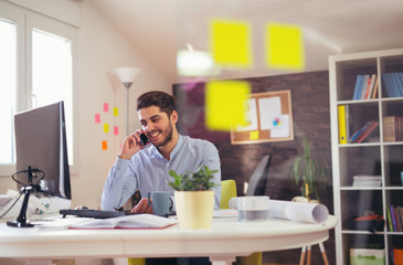 Fototapeta premium Young man talking on phone in office