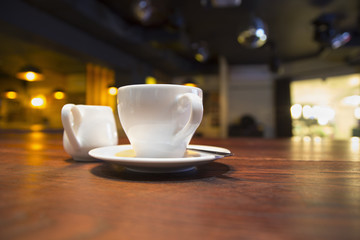 White cup of coffee on a saucer on a table in a dark cafe