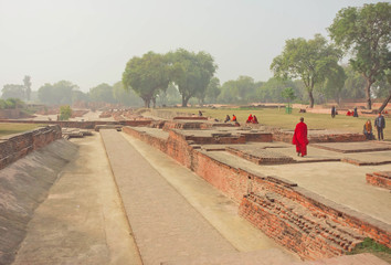 Buddhist monk in red dress walking past ruined temple