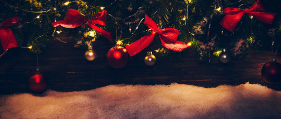 Christmas garland with red bows, ornaments and Christmas lights covered in snow