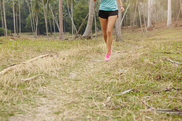 Sports and healthy lifestyle concept. Cropped view of tanned female jogger in sportswear and pink sneakers training in rural area. Athletic girl jogging on trail in countryside preparing for marathon