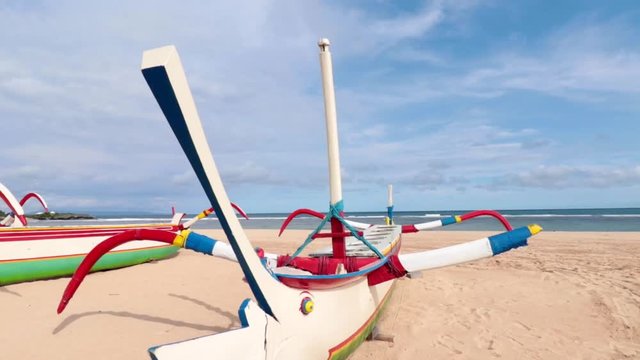 Wooden colorful fishing boat on the beach with blue sky. Nusa Dua, Bali, Indonesia. Slow motion.