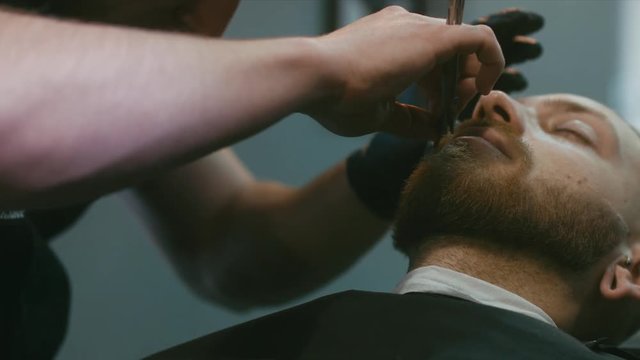 Young hipster Caucasian man during beard and mustache grooming in modern barber shop. 4K UHD RAW edited footage