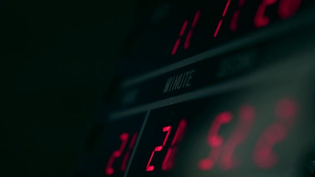 Digital clock in dark room with red glowing digits. Time measurement and electronic technology concepts. 4K video