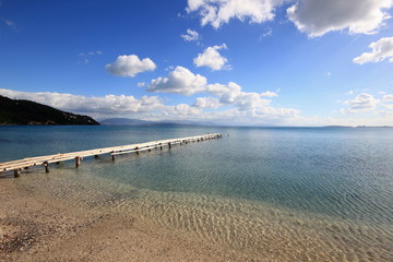 wooden pier of sandy beach into blue sea with no one