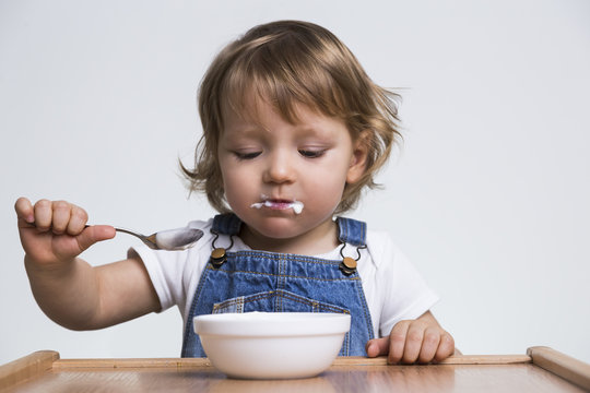 Concentrated Little Boy Eating His Porridge From White Bowl With A Spoon. Concept Of An Independant Baby