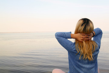 The young girl meditates on the beach sitting on the shore of th