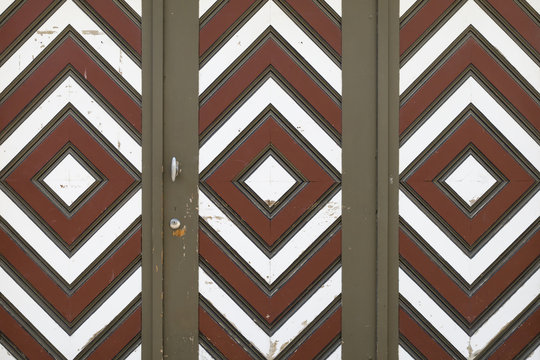A wooden garage door with diamond pattern painted in brown, white and red color