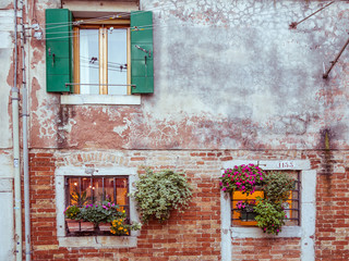 Fototapeta na wymiar Picturesque windows with shutters and flowers in Venice, Italy