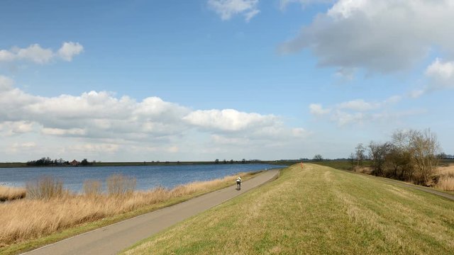 A lone bicyclist rides on a beautiful day across a dike in Holland.
