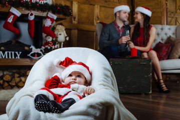 Little child on the foreground in the focus. His happy parents on the background in unfocus. Christmas night.