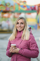 young woman drinking coffee on a background of amusement park