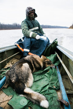 Male hunter swims on a boat with a hunting dog. Cold weather. A man dressed in a warm jacket and hat. Big gray dog Laika.