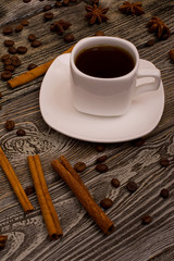 Small white cup of coffee, cinnamon sticks, cocoa beans, star anise on wooden background