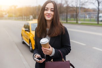 Young brunette standing on street background of passing yellow taxi