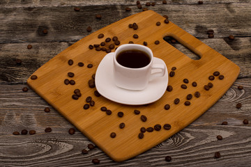 Small cup of coffee, roasted coffee beans on wooden background
