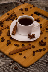 Small white cup of coffee, cinnamon sticks, star anise on wooden background