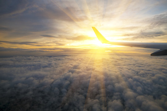Wing of an airplane flying above the sunriseclouds
