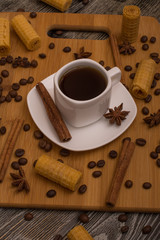 Small white cup of coffee, cinnamon sticks, cocoa beans, star anise and cookies on wooden background