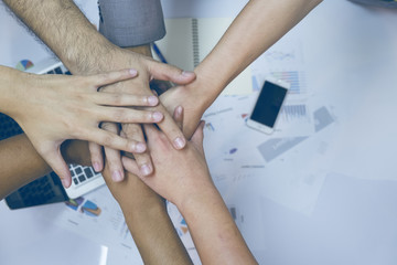 Multiethnic group of young people putting their hands on top of each other. Close up image of young students making a stack of hands with business report background