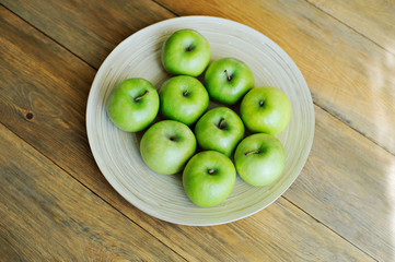 A plate of green apples on wooden background, sunlight.