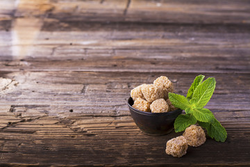 Lump brown cane sugar in a vintage metal dishes with sprig of fresh mint on simple wooden background. The concept natural organic food.