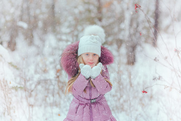 cute little girl blows snow with mittens in winter snowy day