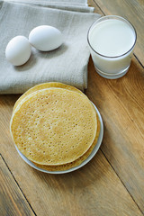 Pancakes and milk, and eggs on a napkin on wooden background, top view. Carnival.