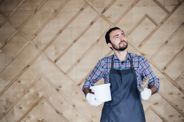 Man with tin of paint and brush looking up on a wooden wall background