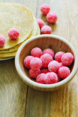 Bright pink round candy in a wooden Cup, in the background, a plate of pancakes.