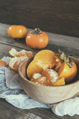 Fresh persimmons and tangerines fruits in bowl on dark wooden background. Coloring and processing photo