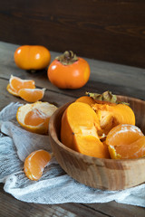 Fresh persimmons and tangerines fruits in bowl on dark wooden background