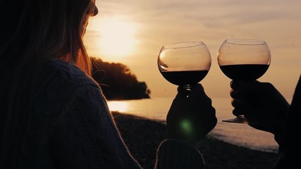 Hands of men and women with glasses of wine, drink wine at sunset on the sea