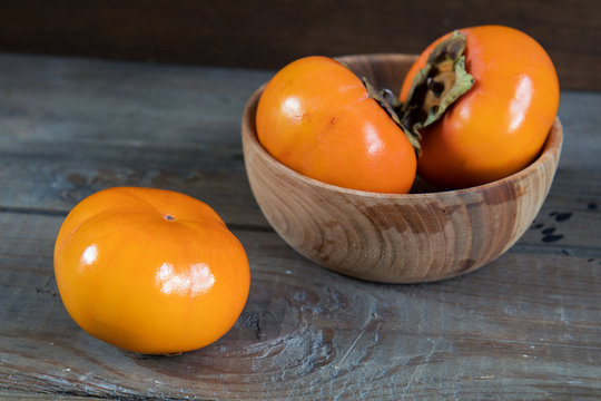 Fresh persimmons fruit in bowl on dark wooden background