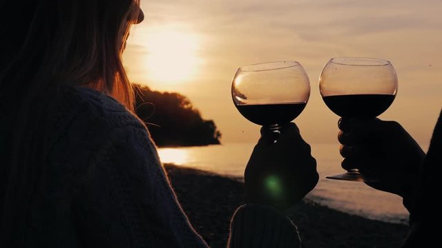 Hands of men and women with glasses of wine, drink wine at sunset on the sea