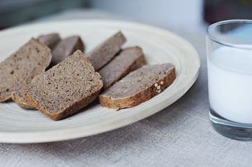 Rye bread on a wooden platter and milk in a glass on a background of rough cloth.