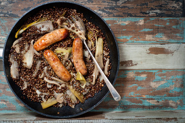 Sausages cooked with lentils, fennel and fresh leeks in a one pot casserole. Served on a rustic wooden table.
