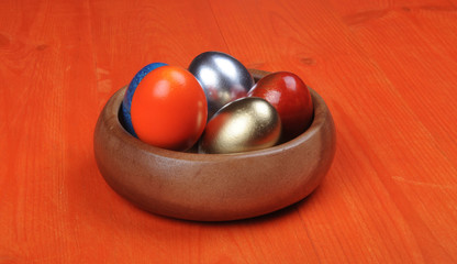 Easter composition. Colorful eggs in a wooden bowl on an orange wooden background. partially tinted photo.
