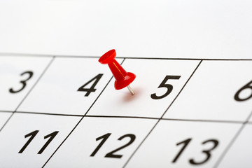 Pin on the date. The fifth day of the month is marked with a red thumbtack. Focus point on the red pin.