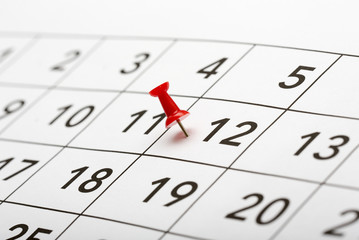 Pin on the date number 12. The twelfth day of the month is marked with a red thumbtack. Focus point on the red pin.
