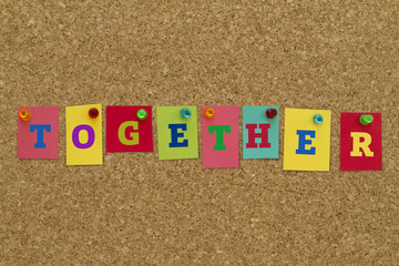 Together word written on colorful sticky notes pinned on cork board.