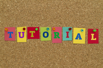 Tutorial word written on colorful sticky notes pinned on cork board.