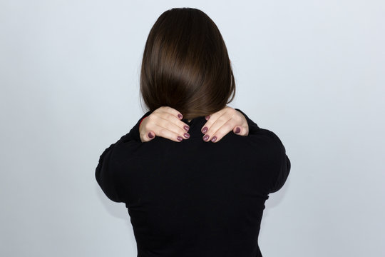 Portrait of a pretty woman in holding her neck in pain and discomfort  standing over gray background
