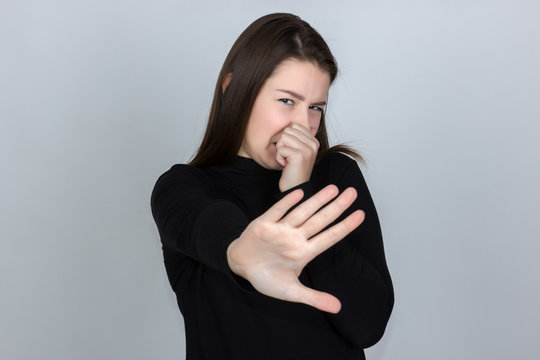 Portrait of a pretty woman  in turtleneck sweater standing over gray background showing stop with one hand and looking at camera with disgust and closes her nose
