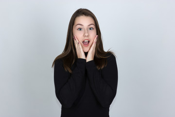 Portrait of a pretty astonished cute girl opening mouth  in turtleneck sweater standing over gray background and looking at camera