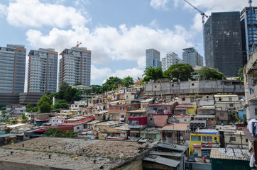 Colorful houses of the poor inhabitants of Luanda, Angola. These ghettos resemble Brazilian favelas. In the background the high rise buildings of the rich build a stark contrast. - obrazy, fototapety, plakaty