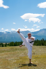 Man in white kimono and black belt training karate on mountain background.